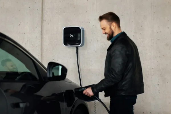 Homme branchant sa voiture électrique à une borne de recharge murale dans un parking de copropriété